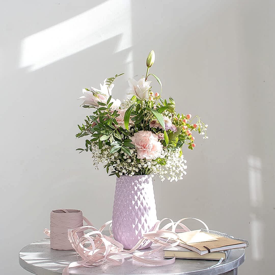 Ramo de flores en tonos rosas decorando una mesa.