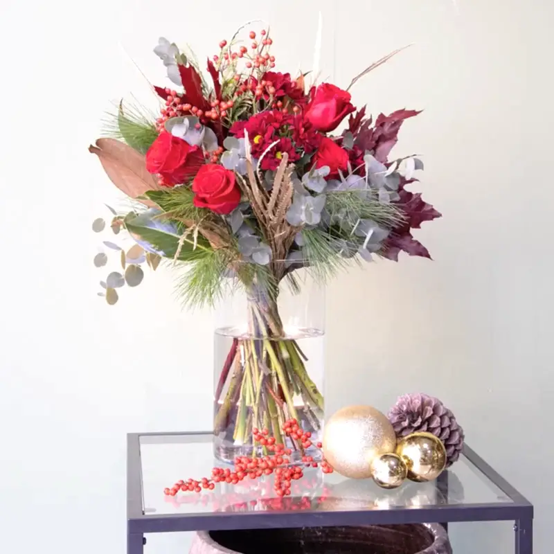 Ramo de flores navideño en tonos rojos y cálidos. Perfecto para regalar a domicilio en Madrid. Presentamos sobre una mesa de salón decorativa.