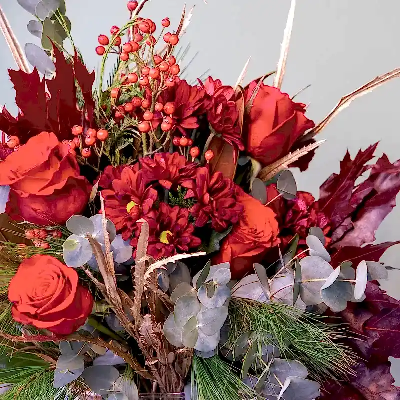 Detalle de Ramo de flores navideño en tonos rojos y cálidos. Perfecto para regalar a domicilio en Madrid.